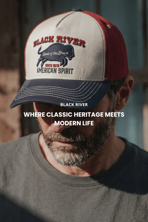 Mężczyzna siedzi na drewnianej skrzynce w studiu i nosi klasyczny brązowy kapelusz kowbojski z filcu z szerokim rondem, ciemną dżinsową koszulę i dżinsy.